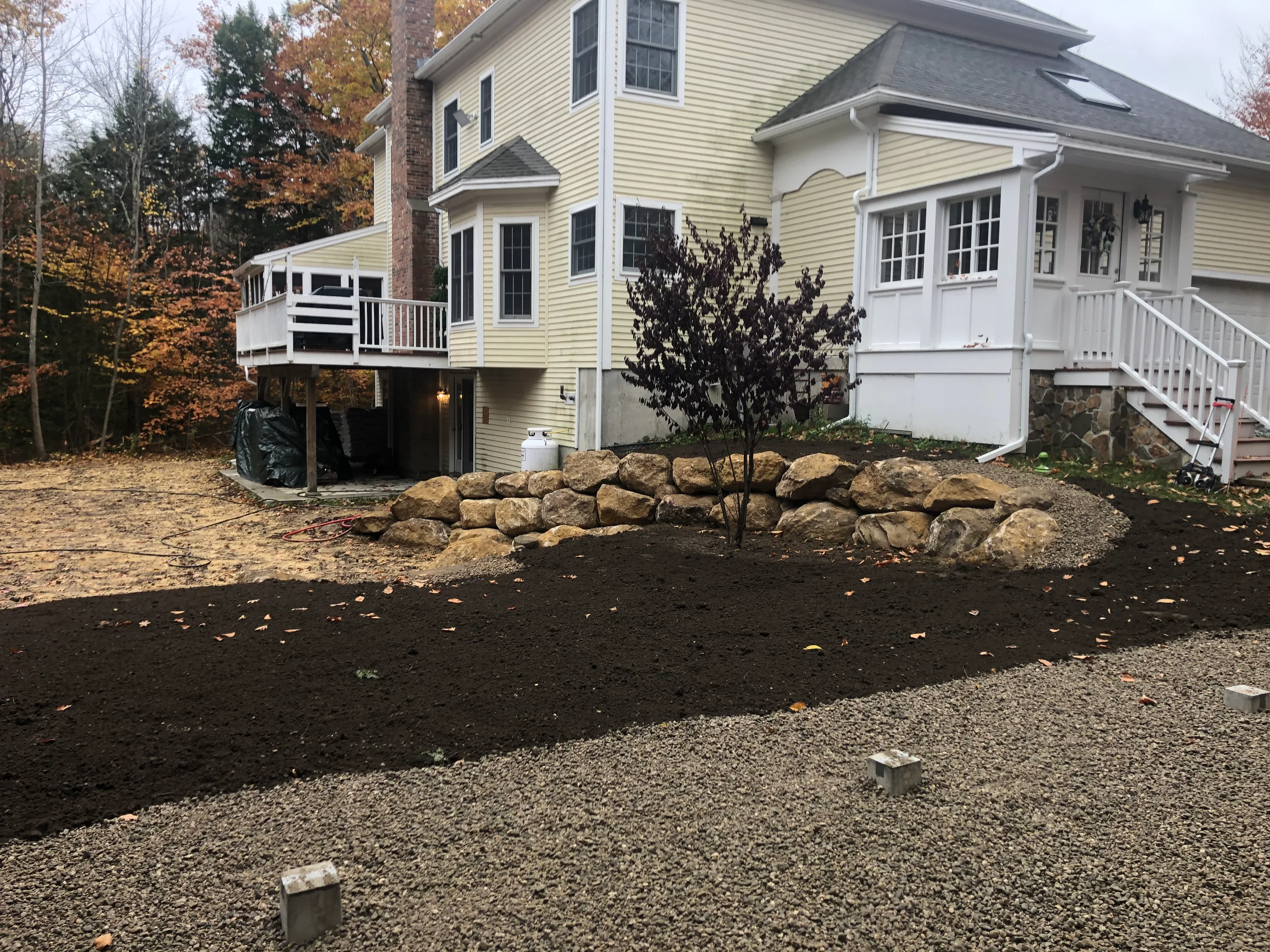Excavated residential yard with crushed stone base, dark topsoil, and stacked boulder landscape edging