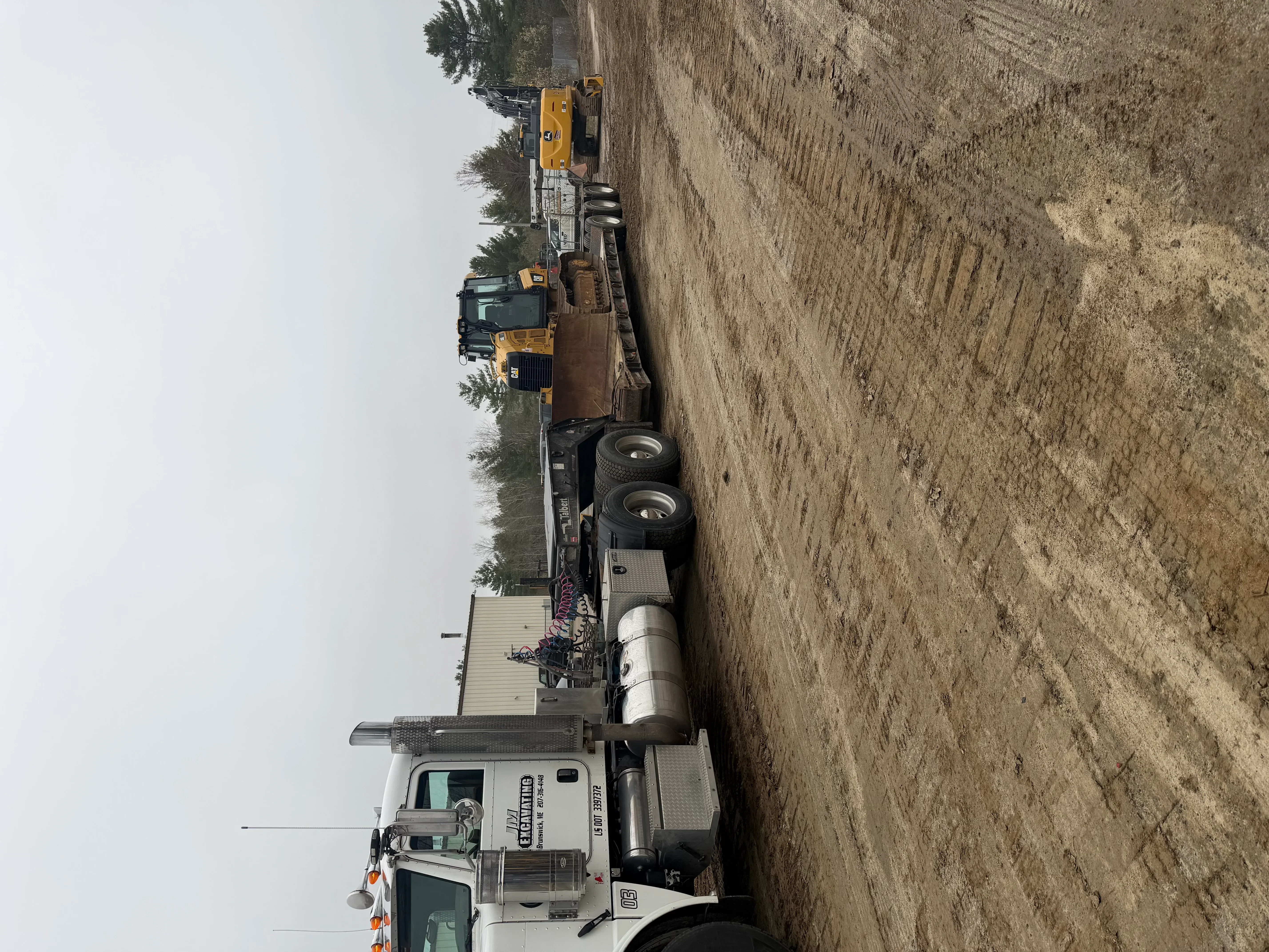 Dump truck with pneumatic tanker trailer on dirt road, aggregate hauling equipment