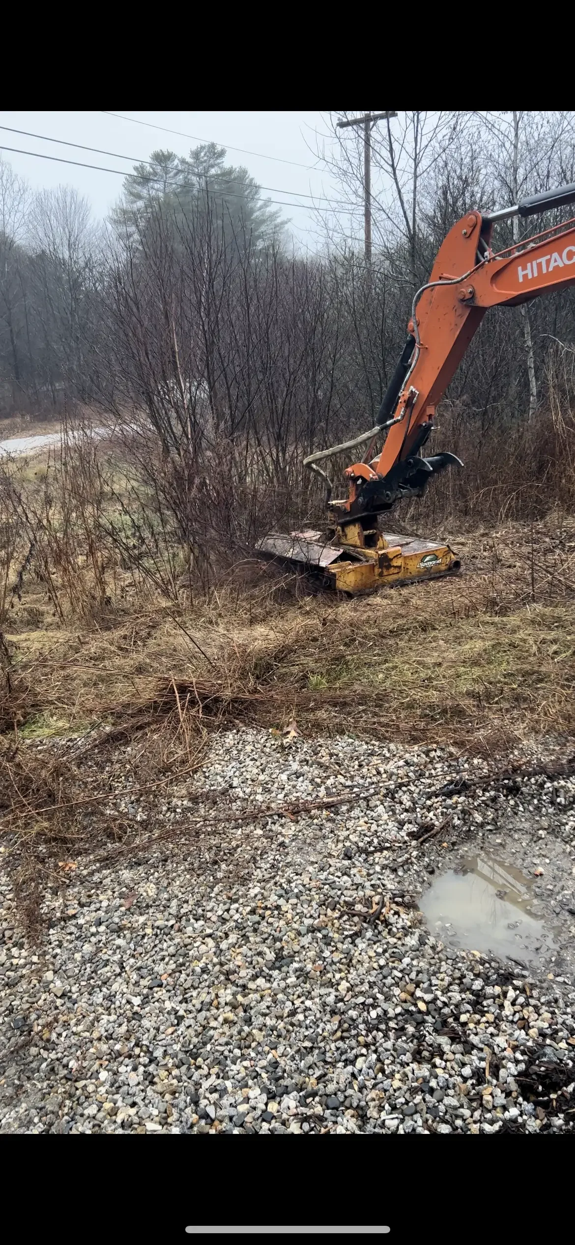 Hitachi excavator clearing brush and vegetation from wooded site with gravel base material