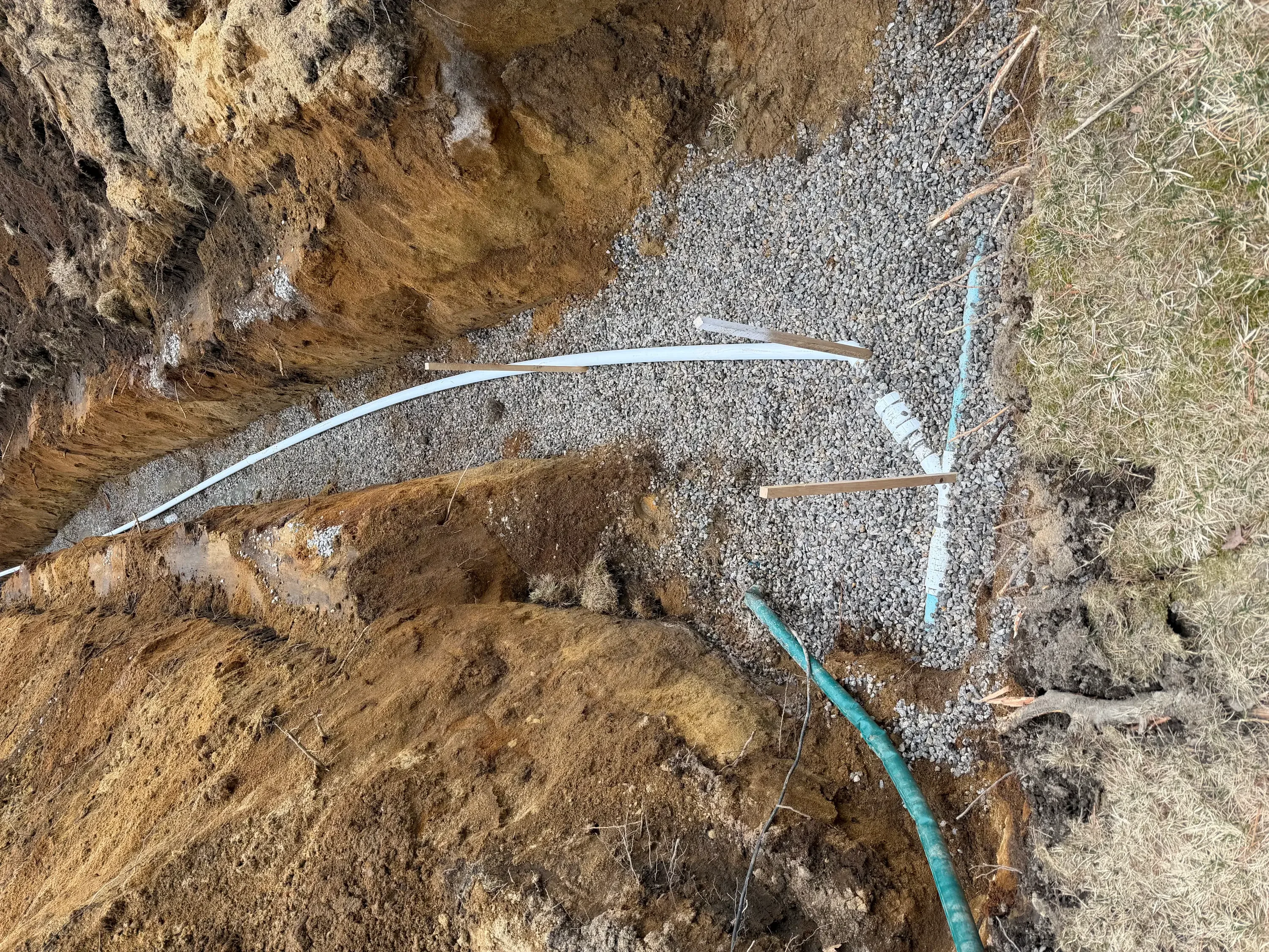 Utility trench with white PVC and blue polyethylene pipes in gravel base, compacted soil walls