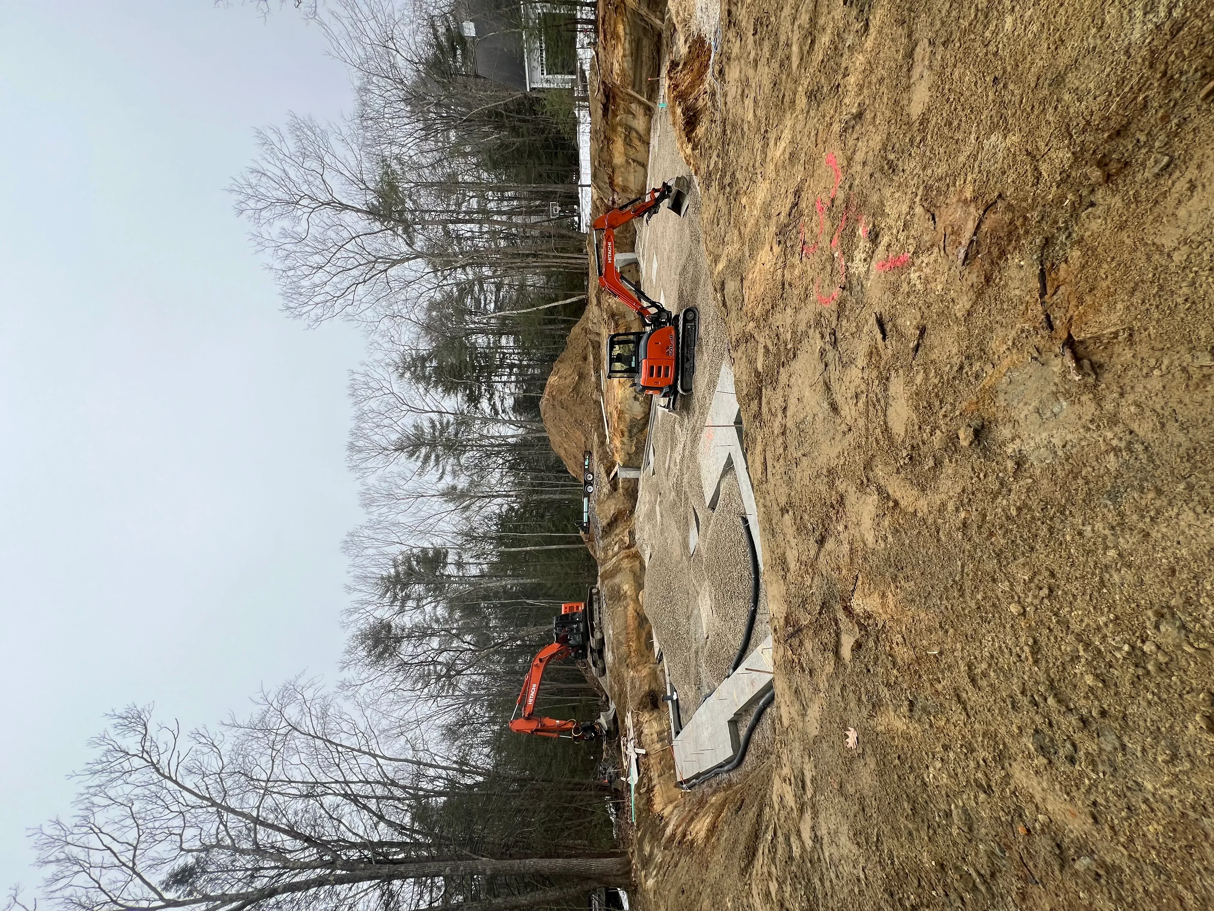 Red excavator on dirt site with concrete pad and graded driveway area