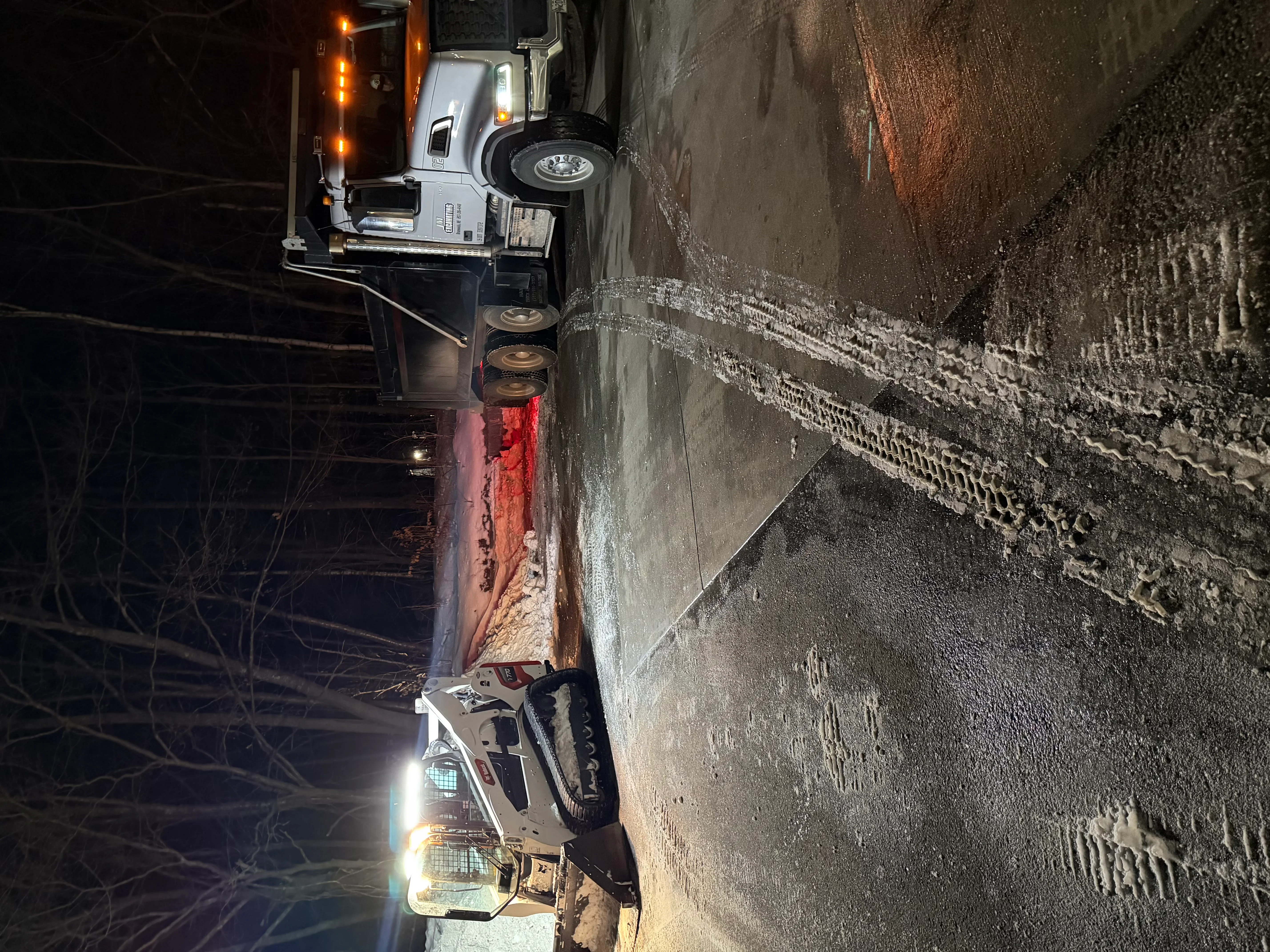 Spreader truck applying salt or sand to snow-covered road at night
