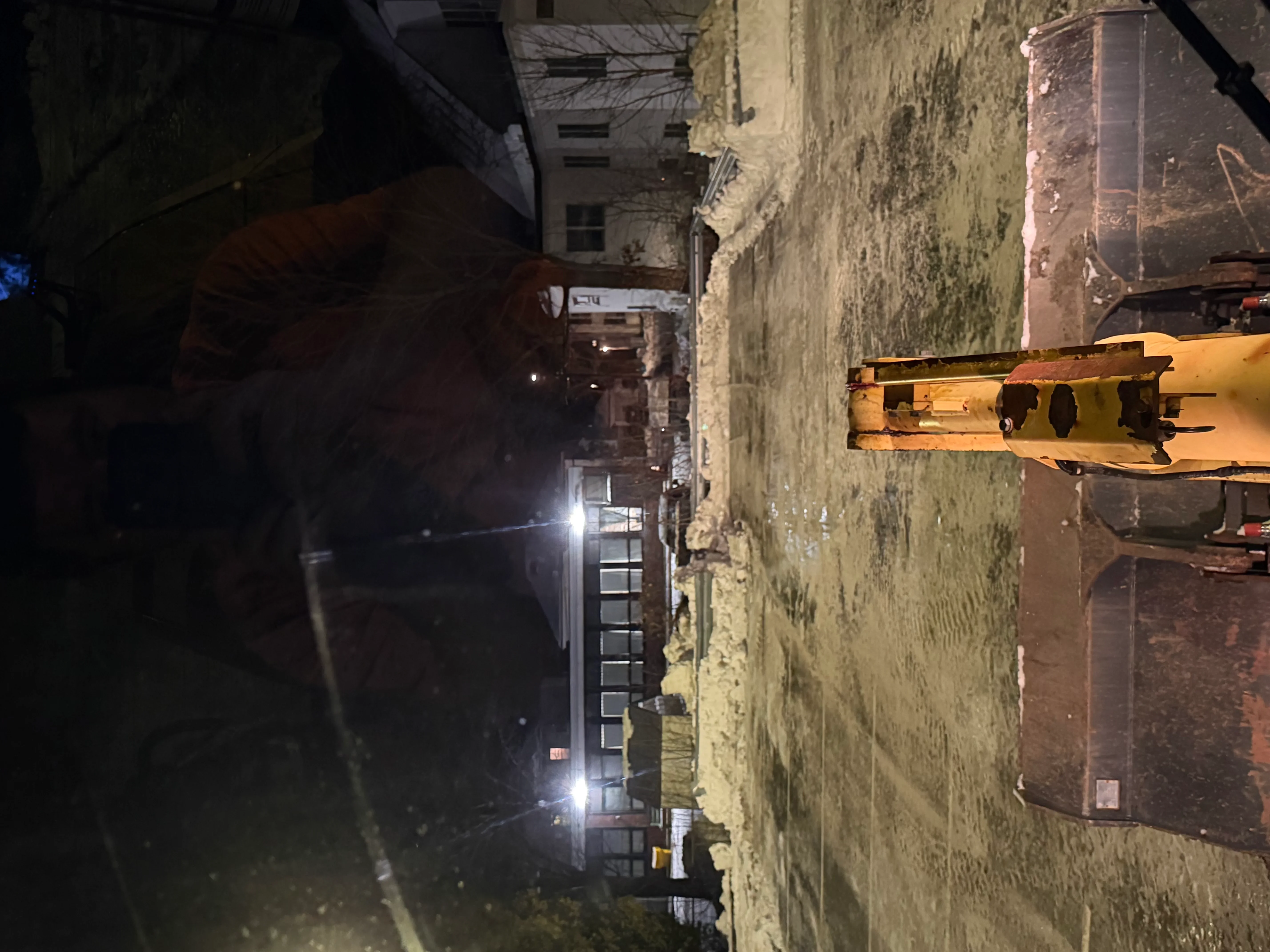 Yellow excavator in urban alley with aged brick buildings and nighttime lighting