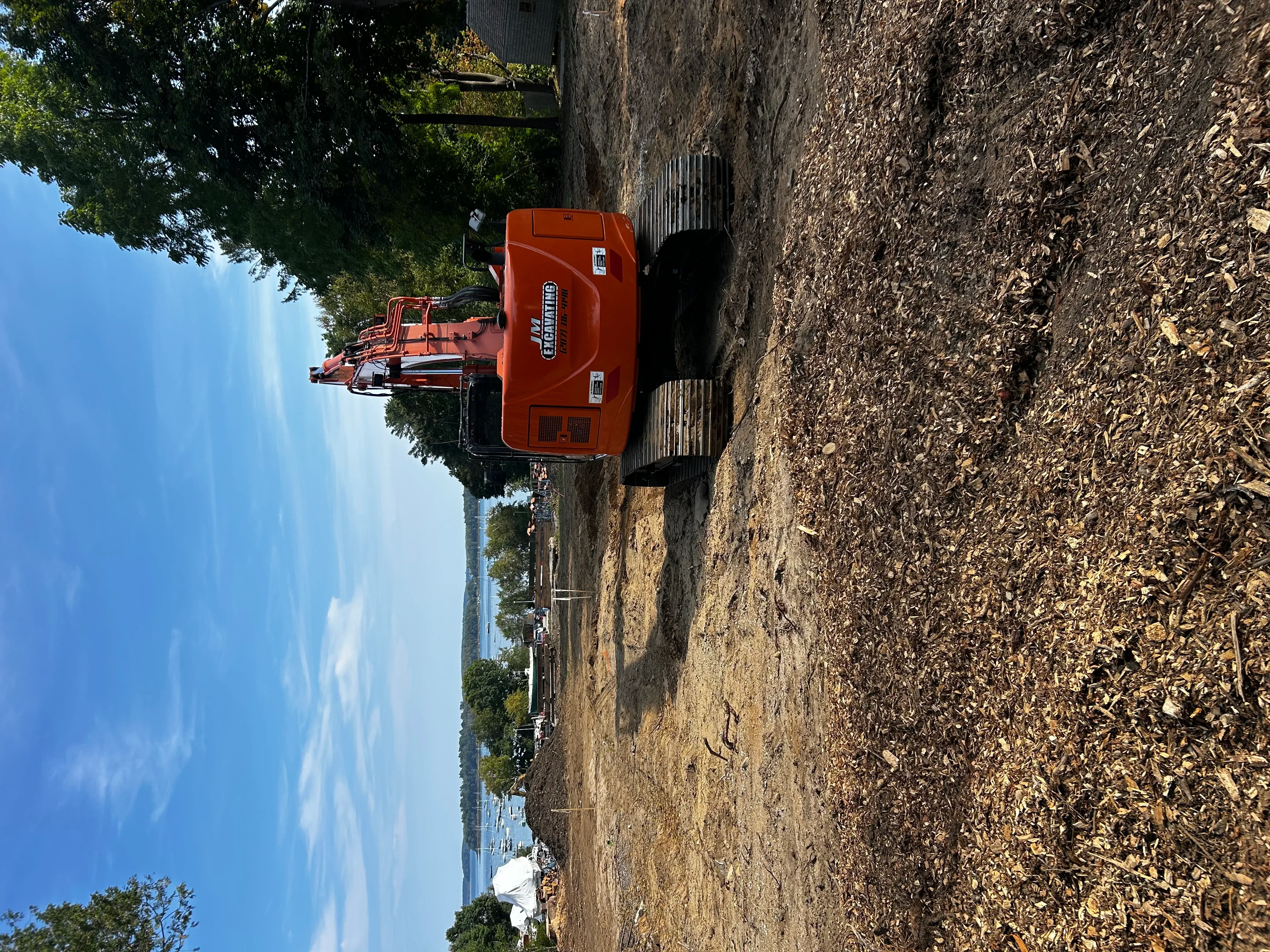 Red excavator on graded dirt driveway with compacted soil and wooden fence