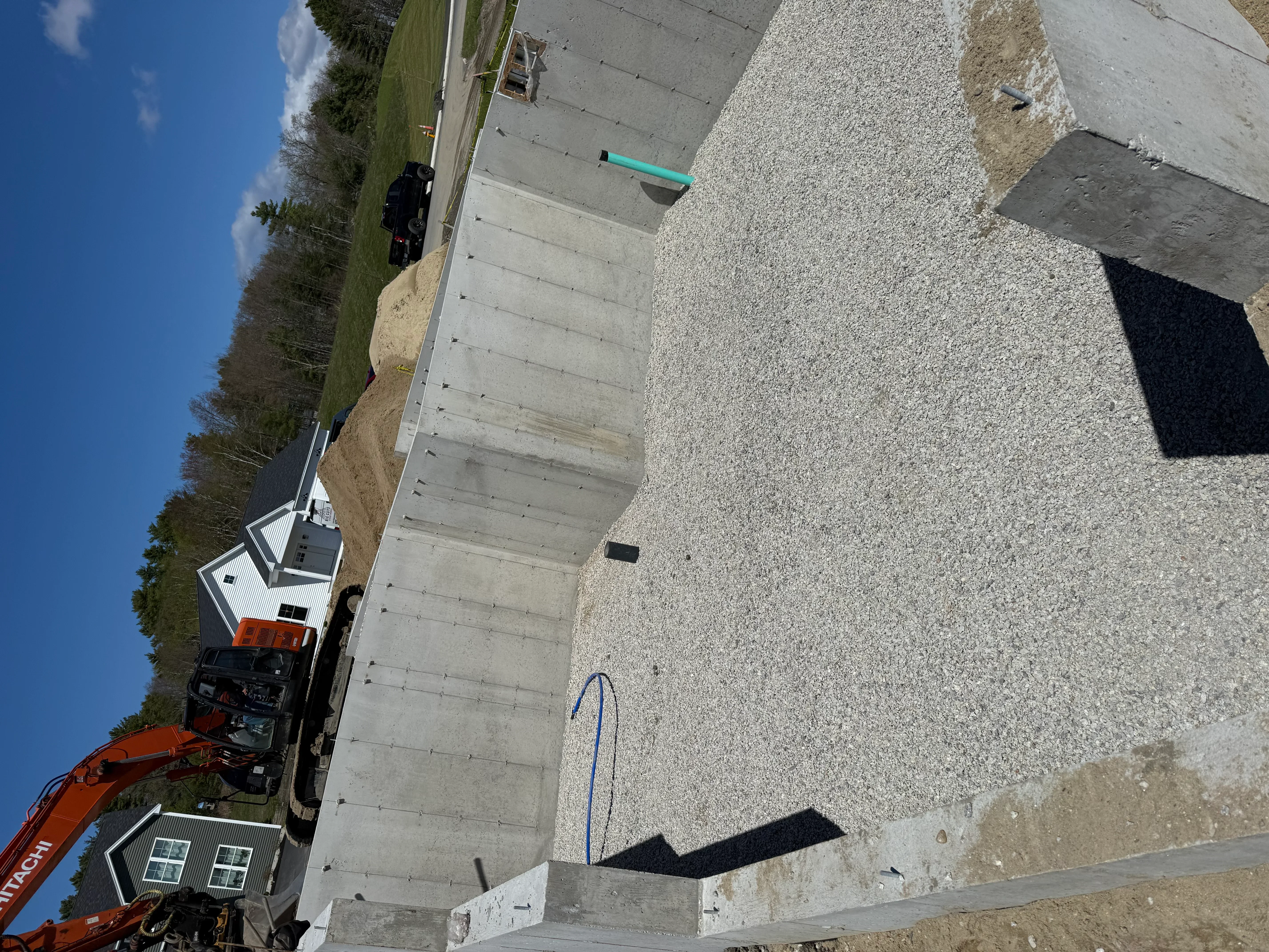 Excavated residential lot with gravel base, concrete foundation pad, and heavy equipment on-site