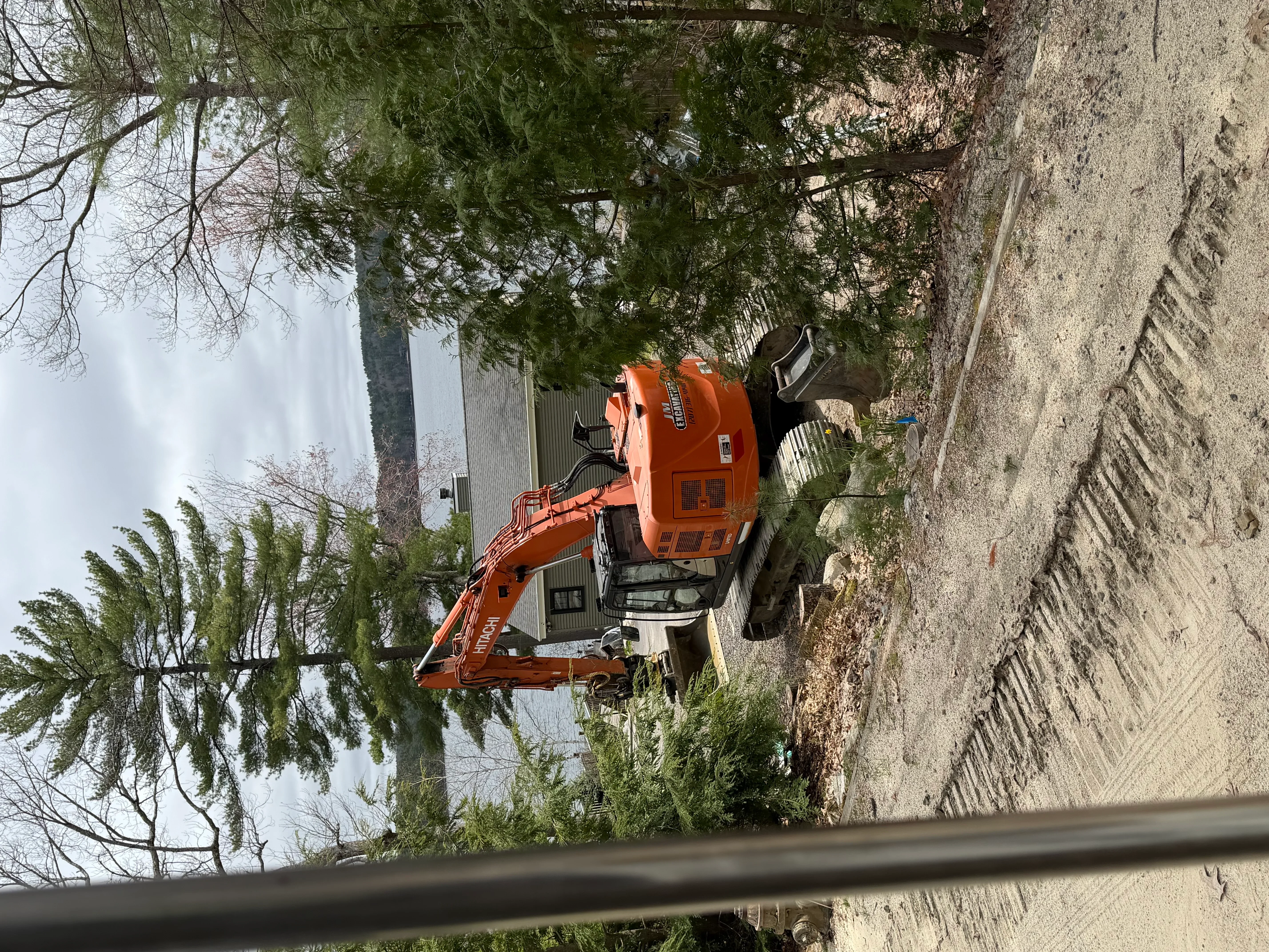 Orange tracked excavator removing concrete driveway material near residential property