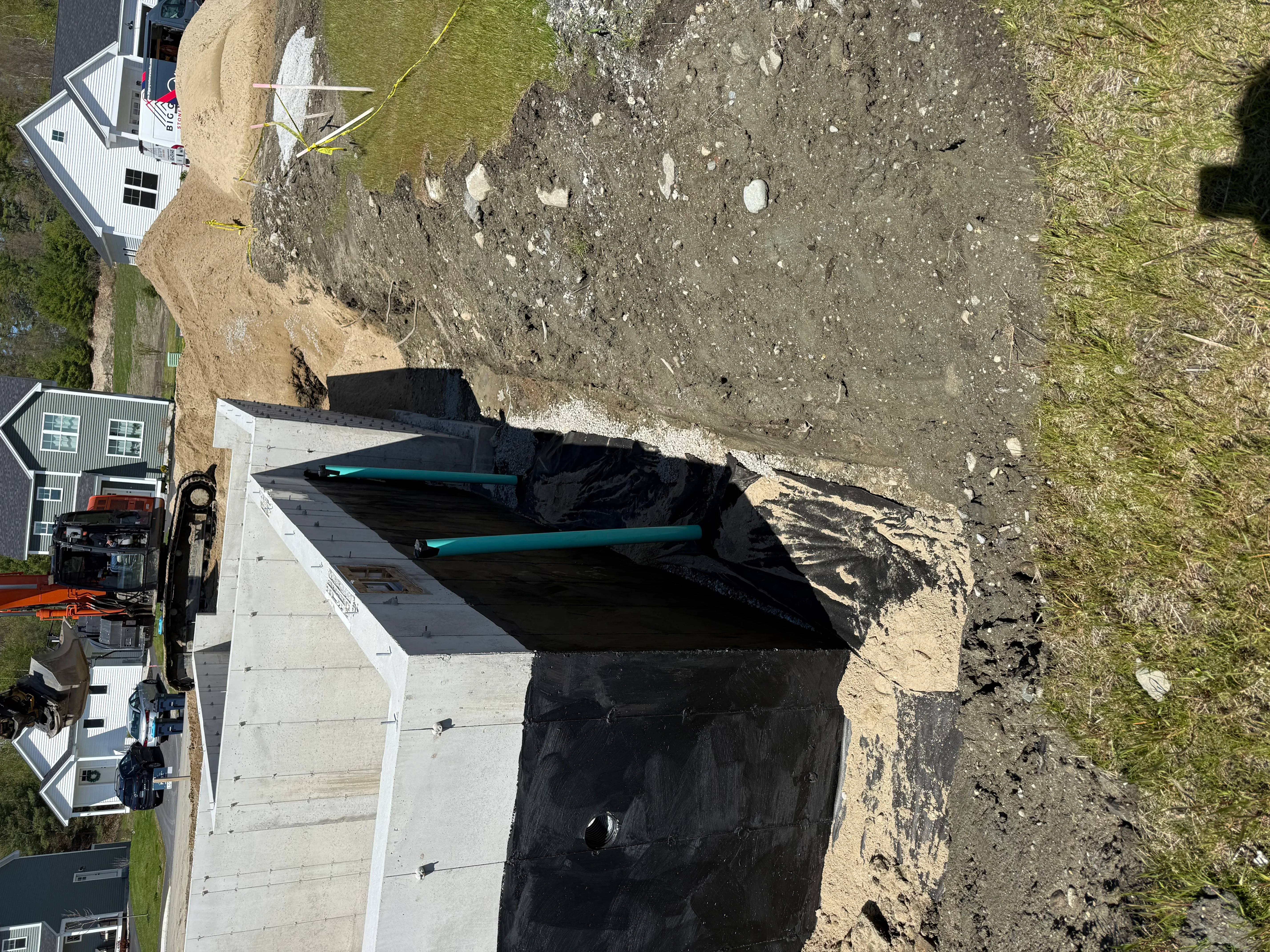 Aerial view of excavated driveway site with black landscape fabric and turquoise drainage pipes installed