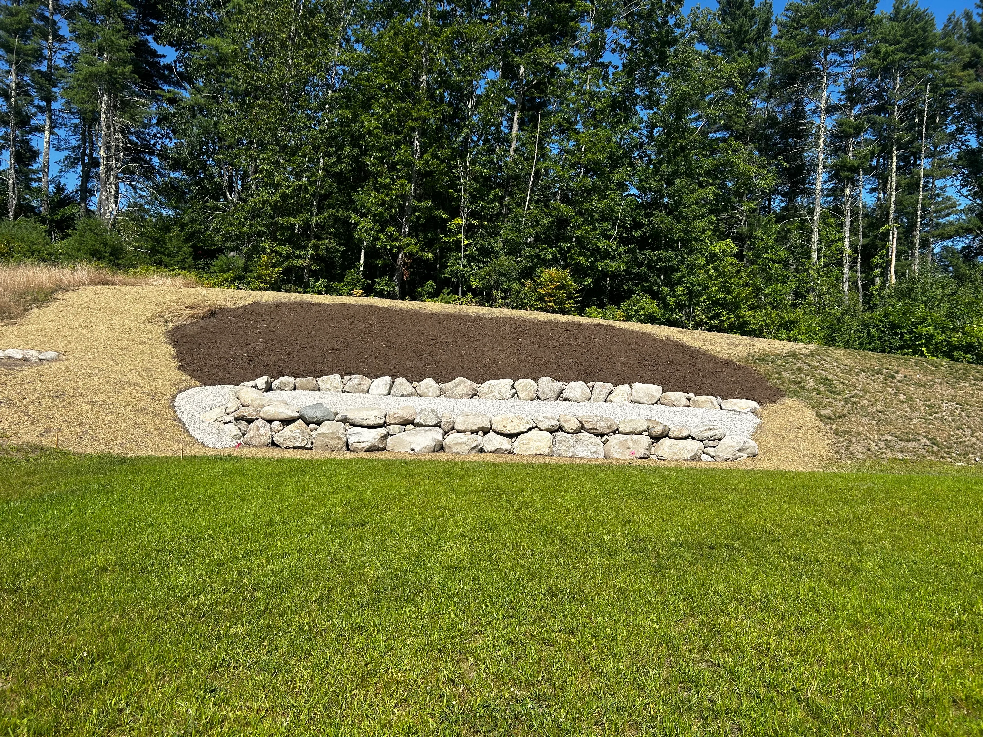 Curved stone retaining wall with stacked granite blocks and graded slope with dark mulch material