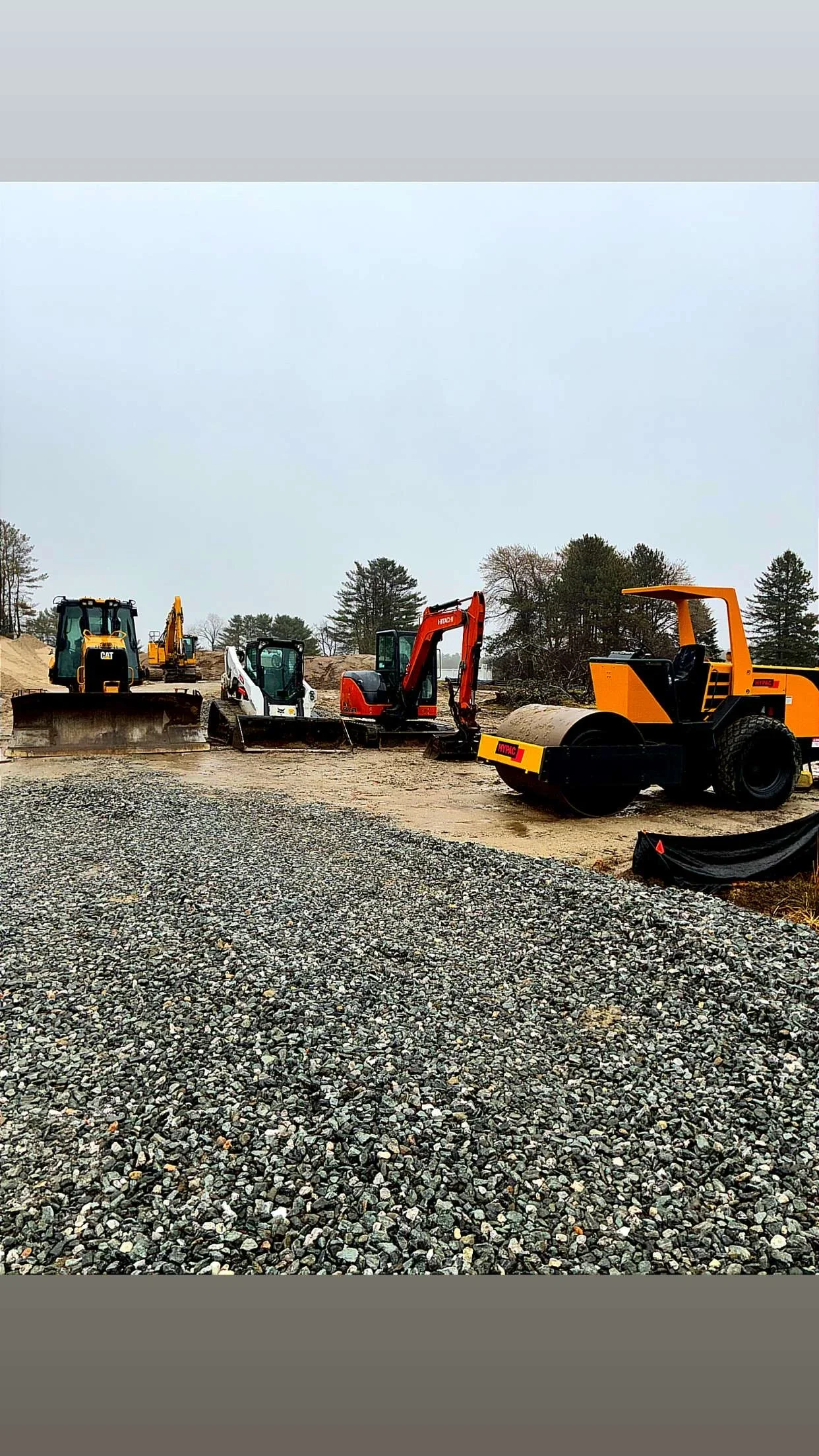 Heavy excavation equipment and orange compactor on gravel base with staged machinery