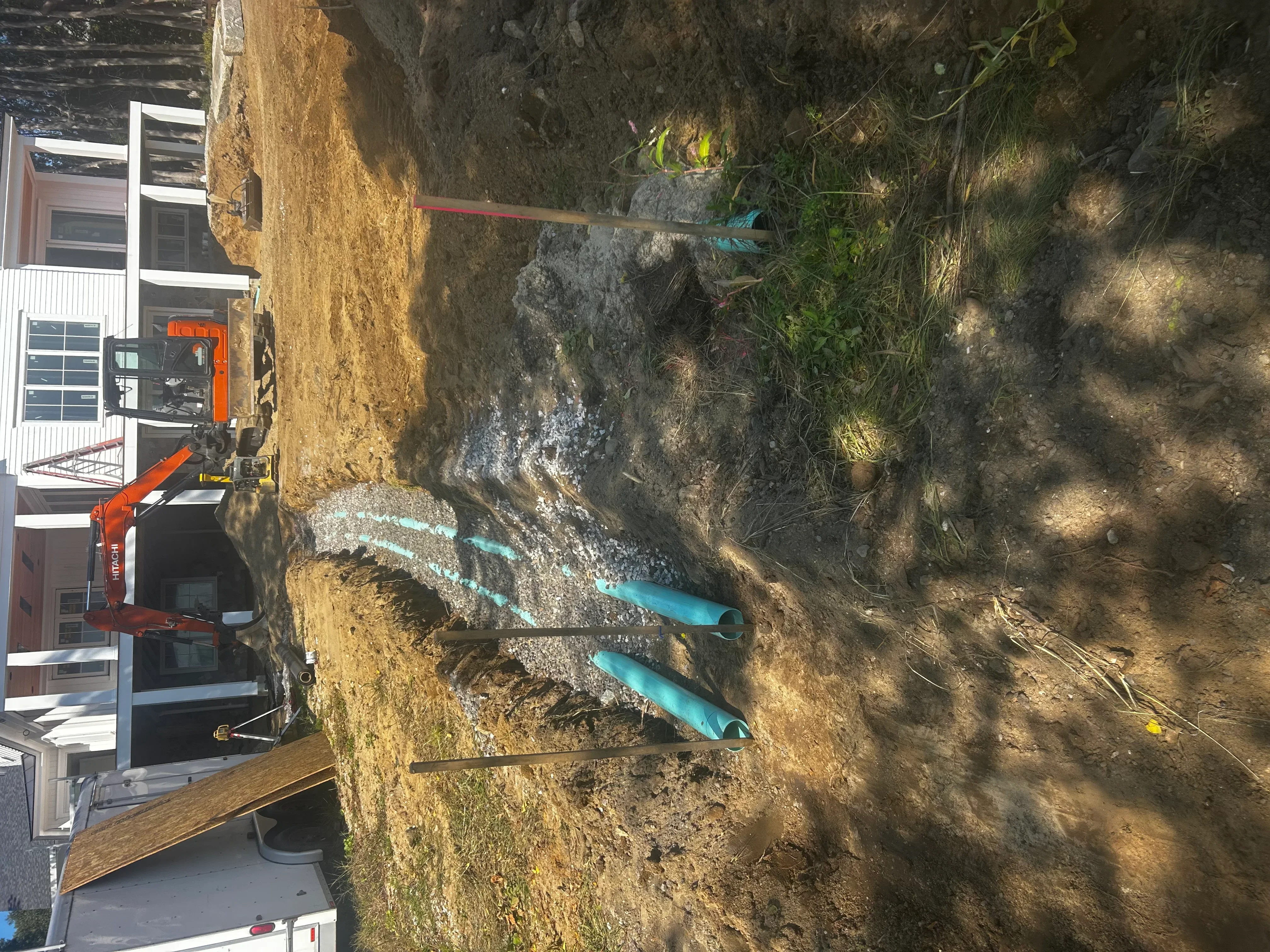 Excavated residential lot with exposed soil, grading work, and heavy equipment on sloped terrain