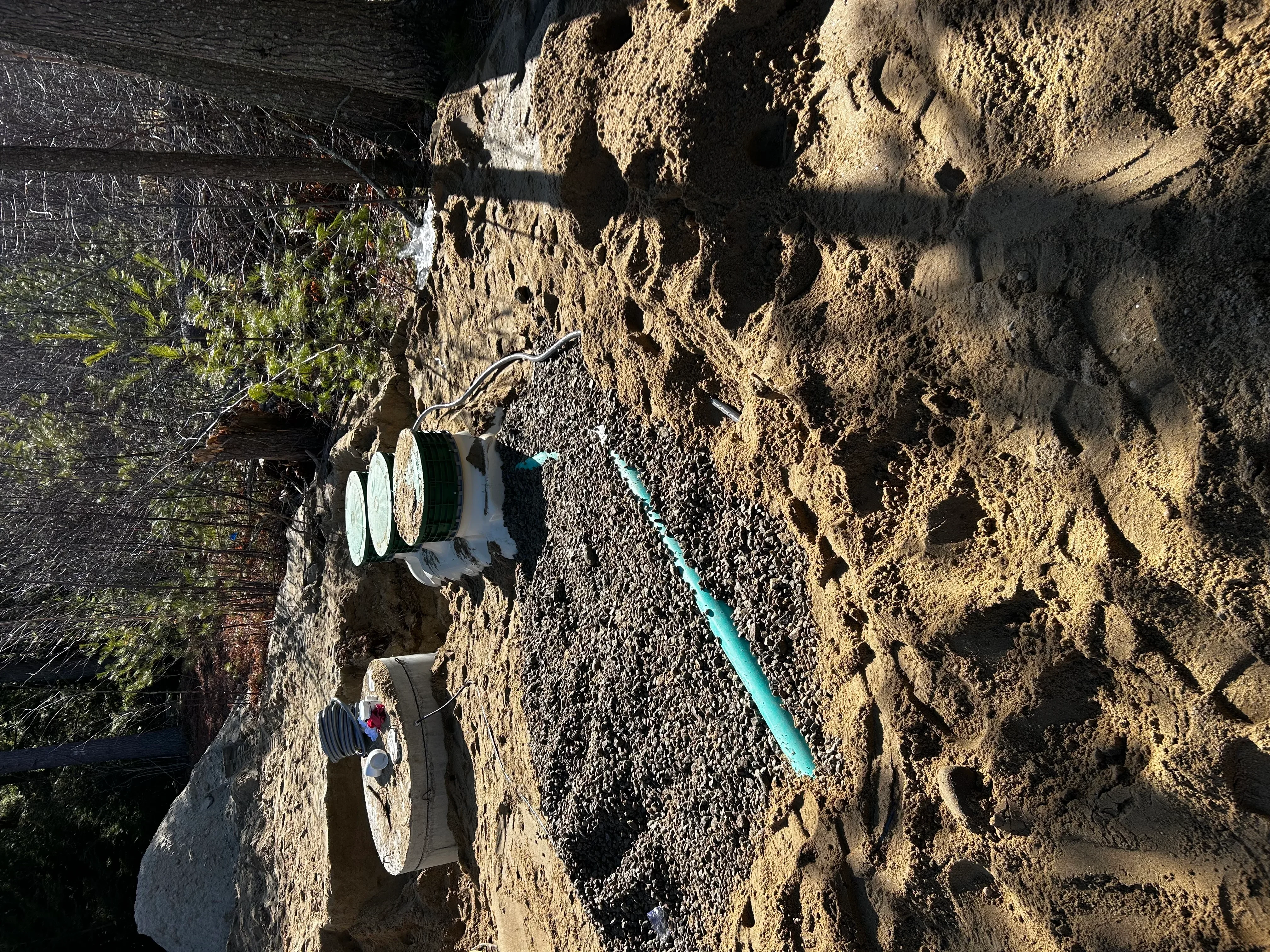 Blue PVC drainage pipe installed in excavated trench with compacted gravel base and graded subgrade